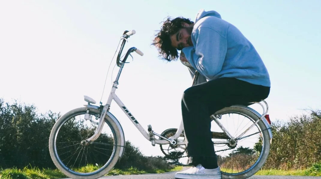 Jeune homme en sweat assis sur le porte bagage d'un vélo