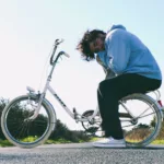 Jeune homme en sweat assis sur le porte bagage d'un vélo