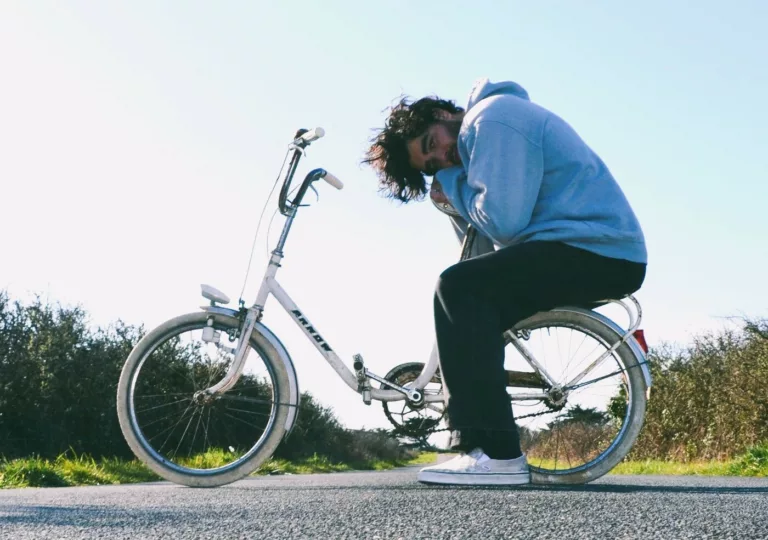 Jeune homme en sweat assis sur le porte bagage d'un vélo
